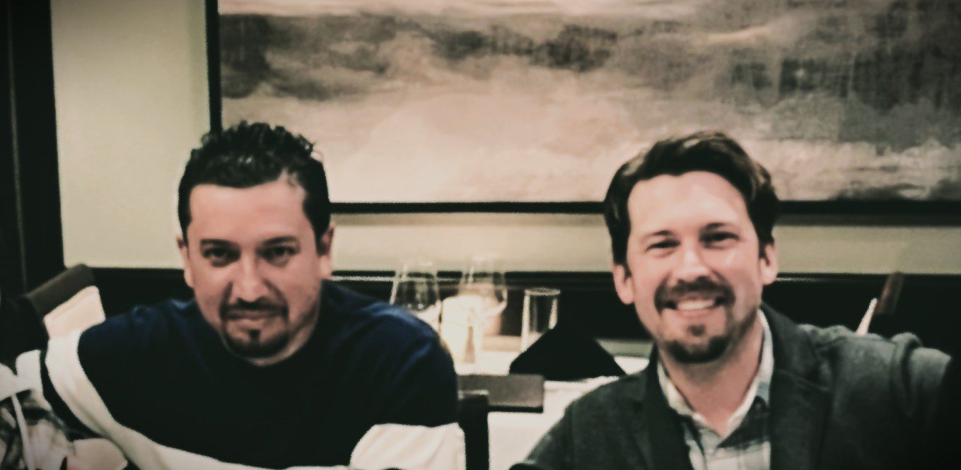 Two men sitting indoors with a blurred background.